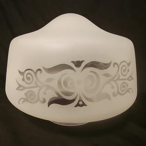 May include: Frosted white glass lampshade with a decorative etched floral design. The lampshade has a rounded top and a flared bottom. The etched design features swirling patterns and leaf-like shapes.