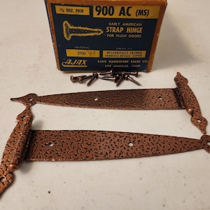 May include: Two Early American strap hinges for flush doors, with a hammered antique copper finish. The hinges are accompanied by a box and screws. The box reads "900 AC (MS)" and "AJAX".