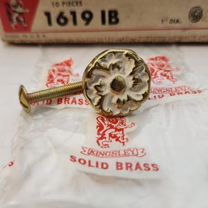 May include: A pack of 10 solid brass knobs with an ivory finish. The knobs are 1 inch in diameter and have a floral design. The packaging includes the text "SOLID BRASS KNOB", "IVORY BRASS FINISH", "10 PIECES", "1619 IB", and "1" DIA."