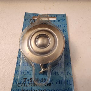 May include: A silver-colored door knob with a circular design, packaged on a blue and white card. The card has the text "Galleon Silver" and "Priced on back".