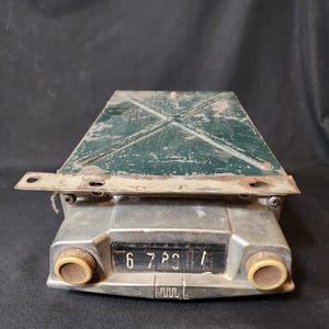 May include: Vintage car radio with a green metal casing and a silver face. The radio has a dial with numbers 6, 7, 8, 9, 11, and 15. The radio has two knobs on the sides.