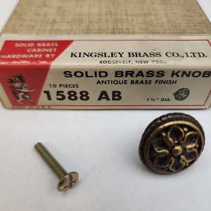 May include: A solid brass cabinet knob with an antique brass finish. The knob is 1 1/2 inches in diameter and comes with a screw. The box says "Kingsley Brass Co., Ltd. Roosevelt, New York" and "Solid Brass Knob Antique Brass Finish 1588 AB 1 1/2" DIA."