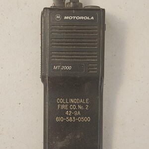 May include: A black Motorola MT 2000 two-way radio. The radio has the Motorola logo and the text "MT 2000". Below the model number is the text "Collingdale Fire Co. No. 2 42-9A 610-583-0500".