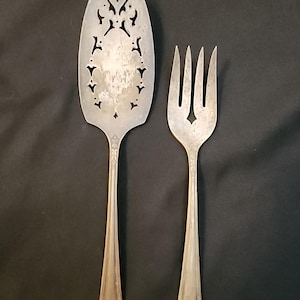 May include: Silver-colored vintage cake server and serving fork set. The cake server has a decorative, pierced design on the blade. The fork has four tines and a matching handle. Both pieces have a classic, elegant look.