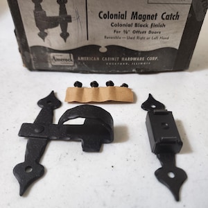 May include: Black metal magnetic door catch with a colonial style design. The catch is reversible and can be used for right or left-hand doors. The package includes screws and instructions. E8555 Colonial Magnet Catch. American Cabinet Hardware Corp. Rockford, Illinois.