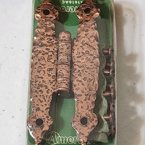 May include: A package of Amerock cabinet hardware. The set includes two decorative hinges, a barrel hinge, and several small screws. The hinges and barrel hinge have a hammered copper finish. The package has a green and white label.