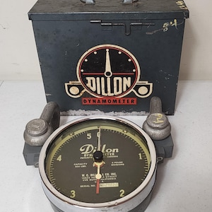 May include: A vintage Dillon dynamometer with a dark green face, black casing, and a metal handle. The gauge reads up to 500 lbs. The accompanying metal box has the Dillon logo and a handle.