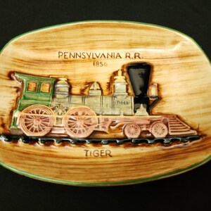 May include: A ceramic wall plaque featuring a vintage Pennsylvania Railroad steam locomotive with the words "Pennsylvania R.R. 1856" and "Tiger" on the plaque.
