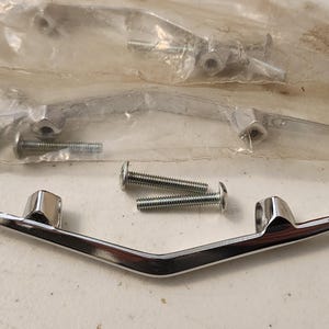 May include: A set of chrome-finished automotive trim pieces, each with a V-shaped design and mounting hardware. The image shows two pieces, along with several screws and nuts, some still in a plastic bag.