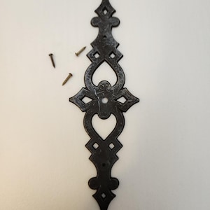 May include: Black metal decorative accent piece with a heart-shaped cutout and intricate design. The accent piece has a distressed finish and comes with two small screws.