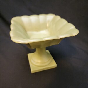 May include: A small, light green ceramic pedestal bowl with a fluted rim and a square base.