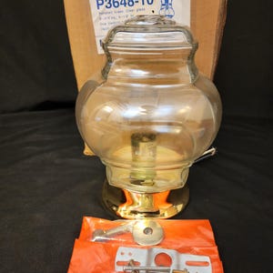 May include: A clear glass and polished brass light fixture with a bulb inside. The fixture is 9 1/2 inches high and comes with mounting hardware in an orange package. The box behind the fixture has the text "P3648-10".