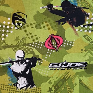 May include: Green camouflage fabric with a repeated pattern of the G.I. Joe logo, a Cobra symbol, and two figures holding swords. The text "G.I. Joe The Rise of Cobra" is printed in white on a black background.