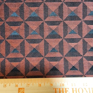 May include: A close-up of a fabric with a geometric pattern of overlapping triangles in shades of brown, black, and teal. The fabric has a textured surface and a subtle sheen.