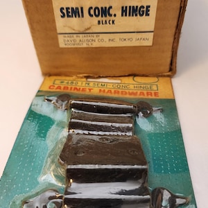 May include: Black semi-concealed cabinet hinge on a green and white card. The card is labeled "CABINET HARDWARE" and the box reads "SEMI CONC. HINGE BLACK". The box also states "MADE IN JAPAN BY DAVID ALLISON CO., INC. TOKYO JAPAN".