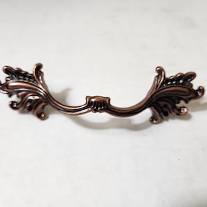 May include: A decorative copper-colored cabinet pull with a floral design.