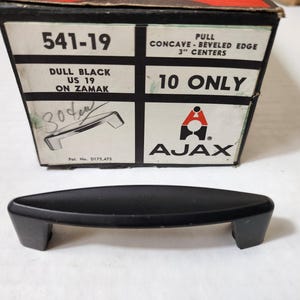 May include: A box of 10 black plastic pull handles with a concave beveled edge. The box is labeled "541-19 Dull Black US 19 on Zamak" and "AJAX 10 ONLY".