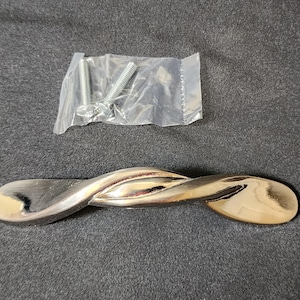 May include: A silver-toned twisted cabinet pull with a smooth, shiny finish. The pull is designed with a curved shape and is approximately 3 inches long.