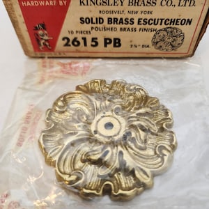May include: A pack of 10 solid brass escutcheons with a polished brass finish. The escutcheons are 2 1/2 inches in diameter and have a decorative floral design. The packaging is labeled "Kingsley Brass Co., Ltd." and "2615 PB".