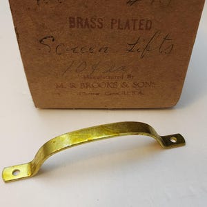 May include: Brass plated screen lift with a gold finish. The lift is labeled "#119 Brass Plated Screen Lifts 104 la Manufactured By M.S. Brooks & Sons Chemex Conn. U.S.A."