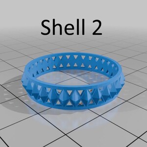 May include: A bright blue ring with a geometric design and the text "Shell 2". The ring features a repeating pattern of triangular shapes. The design is made up of a series of raised, pointed shapes.