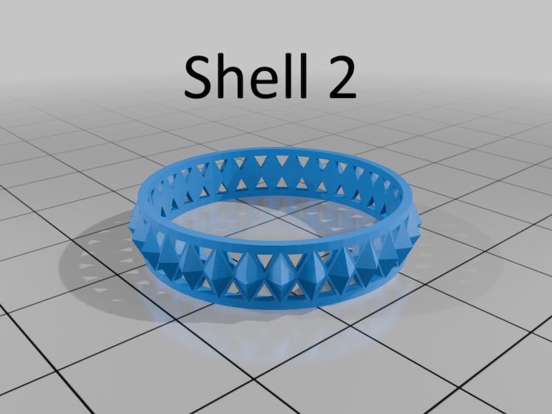 May include: A bright blue ring with a geometric design and the text "Shell 2". The ring features a repeating pattern of triangular shapes. The design is made up of a series of raised, pointed shapes.