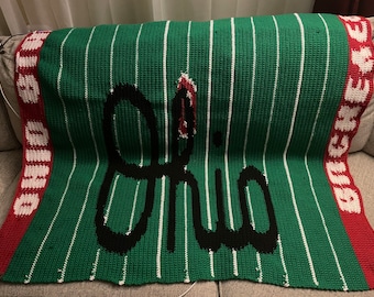 May include: A green and white crocheted blanket with the word "Ohio" in black lettering. The blanket has red and white stripes on the sides with the word "Ohio" repeated on each side.