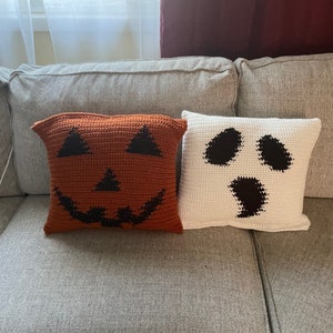 Peut inclure: Deux coussins d'Halloween en crochet, l'un orange avec un visage de citrouille et l'autre blanc avec un visage de fantôme.