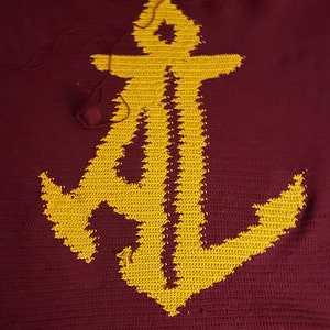May include: A maroon crocheted blanket with a yellow anchor design.