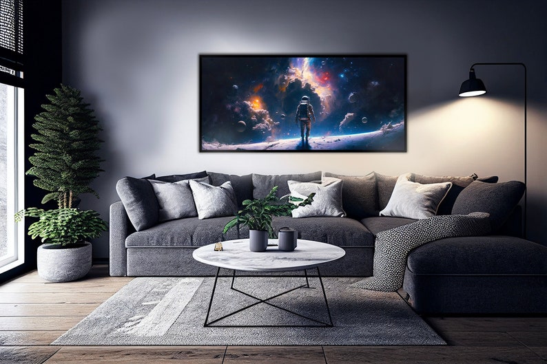 May include: A dark grey sectional sofa with grey cushions in a living room setting. A framed print of an astronaut standing on a planet in space hangs on the wall above the sofa. A small potted plant sits on a white marble coffee table with a black metal frame.