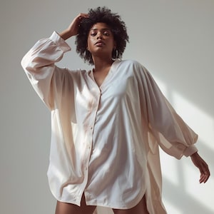 Peut inclure: Une chemise boutonnée ample de couleur pêche claire, avec de longues manches volumineuses. La chemise a un col en V et une coupe décontractée. La chemise est portée par un mannequin. Le tissu est doux et fluide.