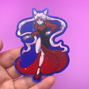 May include: A die-cut sticker featuring a stylized anime character in a red and black dress with long flowing hair. The character is set against a blue background with white stars and a blue outline. The sticker is held by a hand.