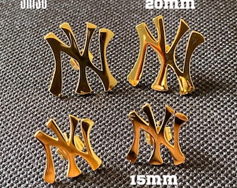 May include: Four gold-colored earrings in the shape of the letters "NY". Two pairs are shown, one pair measuring 20mm and the other 15mm. The word "grise" is printed in the upper left corner.