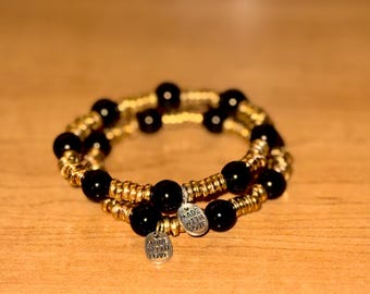May include: Two-toned bracelet with black beads and gold accents. The bracelet has two silver charms that say "Made with Love".