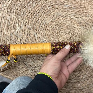 May include: A handcrafted ceremonial pipe with a wooden stem adorned with red and yellow beads. The pipe features a carved wooden turtle head and is embellished with feathers and fur.