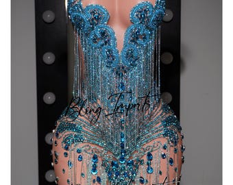 Könnte beinhalten: Ein durchsichtiger blauer Body mit tiefem Ausschnitt und Fransenbesatz. Der Body ist mit Strasssteinen und Perlen besetzt. Der Text "Bling Imports" ist auf dem Kleidungsstück sichtbar.