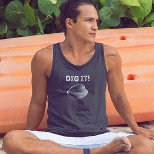 Peut inclure: Un homme portant un débardeur gris foncé avec le texte "DIG IT!" et un graphique de coquille de palourde blanche. Il est assis sur une plage de sable avec un kayak orange vif derrière lui.
