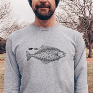 Peut inclure: Un sweat-shirt gris avec une illustration noire et blanche d'un poisson et le texte "For the" imprimé sur le devant.