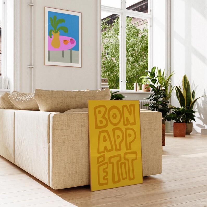 May include: A yellow poster with the text "BON APP&Eacute;TIT" in a bold, orange font. The poster is leaning against a beige couch in a living room.