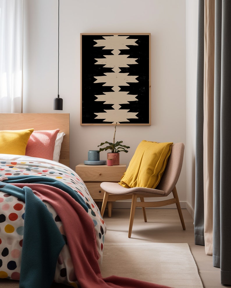 May include: A bedroom with a bed, a chair, a nightstand, and a framed print with a geometric pattern. The bed has a white and colorful polka dot duvet cover, a teal blanket, and a pink throw blanket. The chair is upholstered in beige fabric and has a yellow pillow. The nightstand is made of wood and has a small plant on top. The print is black and white and has a geometric pattern.