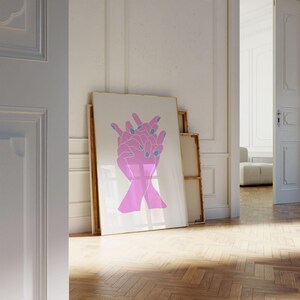 Large trendy poster framed and leaning against a wall. The poster is soft pink hands intertwined with light blue nail polish. The art is a pop art style that would work in mid century modern decor