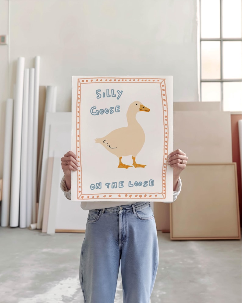 Peut inclure: Une affiche blanche avec une bordure rose et orange. L'affiche pr&eacute;sente une illustration de dessin anim&eacute; d'une oie blanche avec le texte "Silly Goose on the Loose".