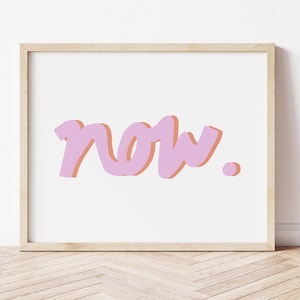 May include: A framed print with the word "now" in a stylized, bubble-letter font. The word is in a light purple color with a peach-colored shadow, set against a white background. The frame is a light wood color.