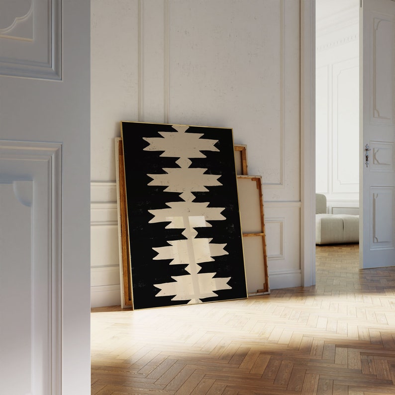 May include: A black and white abstract geometric print framed in a gold frame. The print is leaning against a white wall.