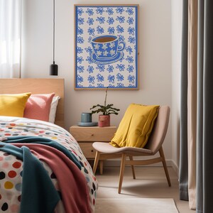 May include: A framed print of a blue teacup with white flowers on a white background with a blue flower pattern. The print is hanging on a white wall in a bedroom with a bed, bedside table, and chair.
