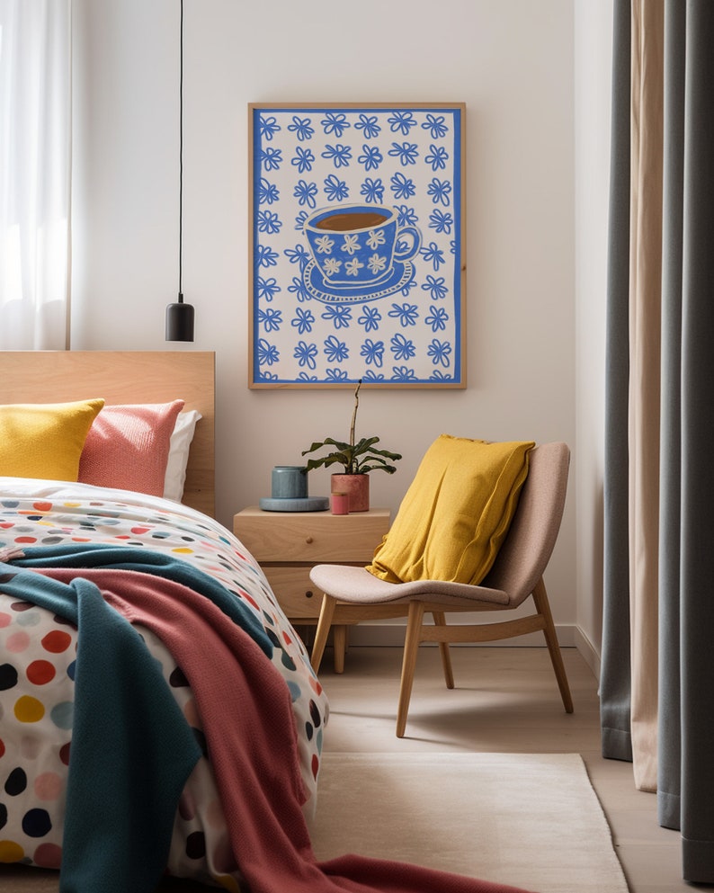 May include: A framed print of a blue teacup with white flowers on a white background with a blue flower pattern. The print is hanging on a white wall in a bedroom with a bed, bedside table, and chair.