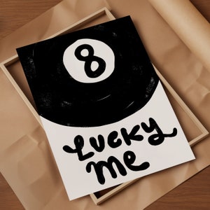 May include: A black and white illustration of a pool ball with the number 8 on it. The text "Lucky Me" is written in a playful, handwritten style below the ball.