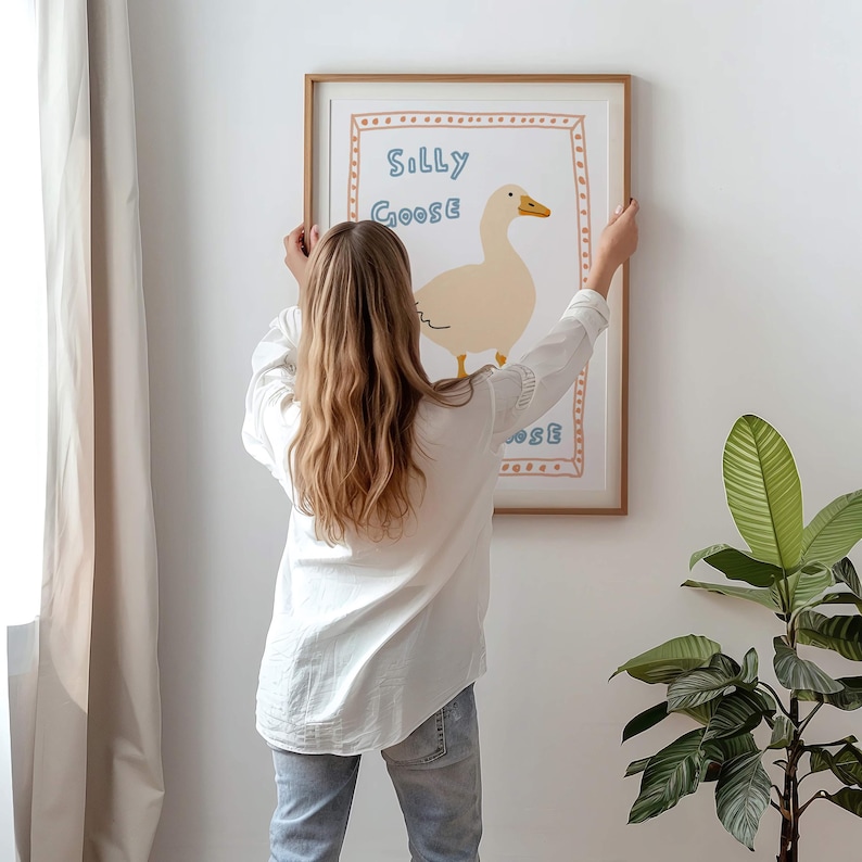 Peut inclure: Une impression encadr&eacute;e avec un fond blanc et une illustration de dessin anim&eacute; d'une oie. Le texte "Silly Goose" est &eacute;crit en lettres bleues et orange.