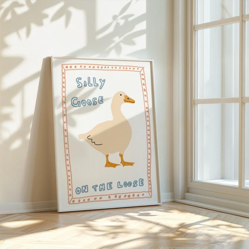Peut inclure: Une impression encadr&eacute;e blanche avec une illustration de dessin anim&eacute; d'une oie blanche aux pieds orange et au bec bleu. Le texte "Silly Goose On The Loose" est &eacute;crit en lettres bleues et orange &agrave; l'int&eacute;rieur d'un cadre &agrave; pois rose et blanc.