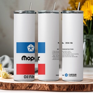 May include: Two white stainless steel tumblers with lids and straws. The tumbler on the left has a blue and red Mopar logo with the text "Oil Filter". The tumbler on the right has instructions for installation and a Chrysler Corporation logo.